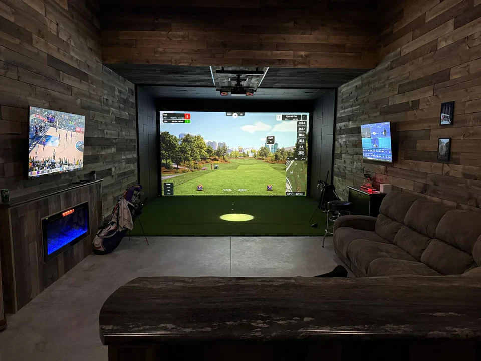 Golfer practicing indoors with a home golf simulator and virtual course screen